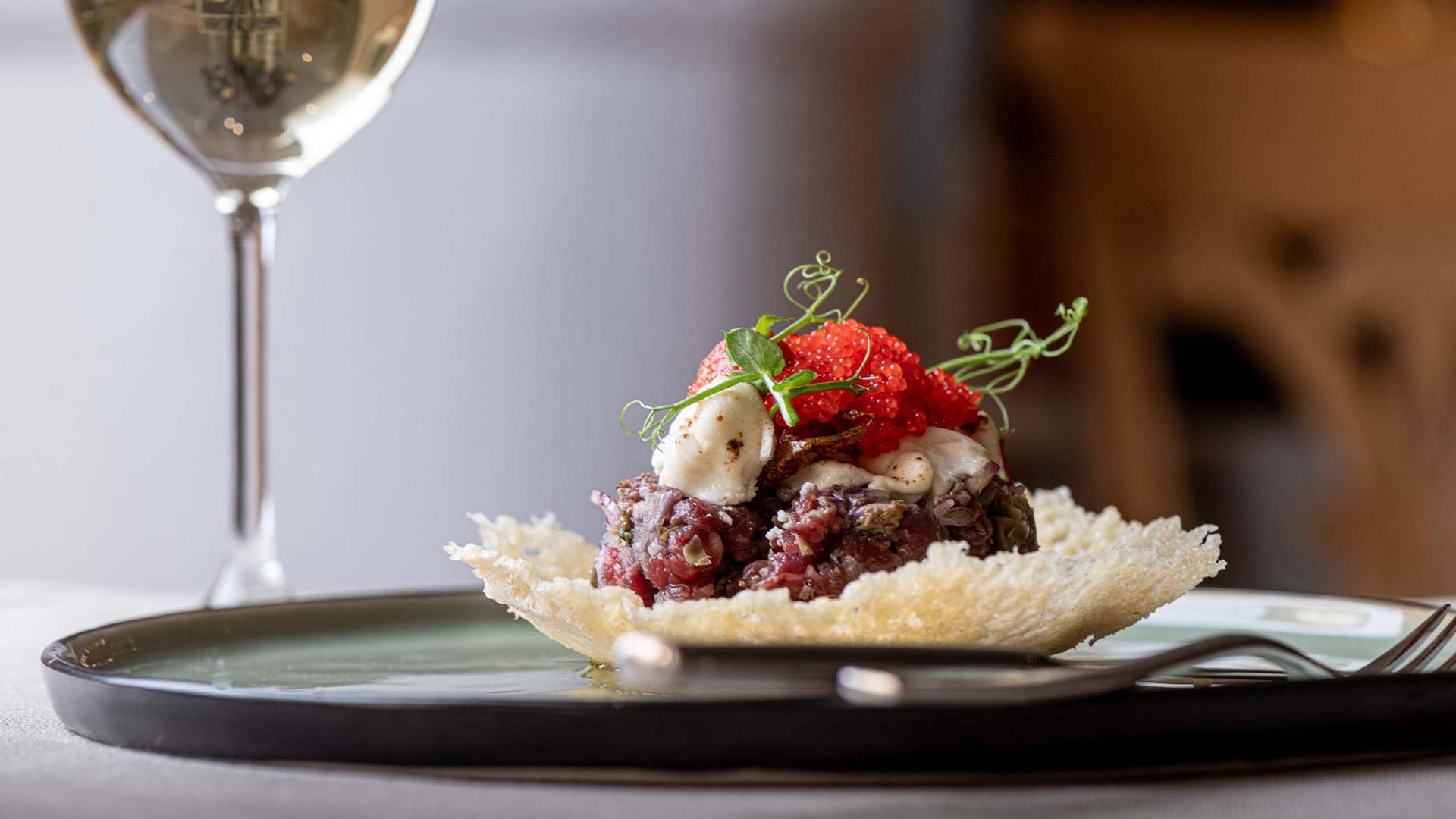 Benessere alpino al nostro albergo in Tirolo Piatto gourmet con carne cruda e uova di pesce su piatto croccante con bicchiere di vino