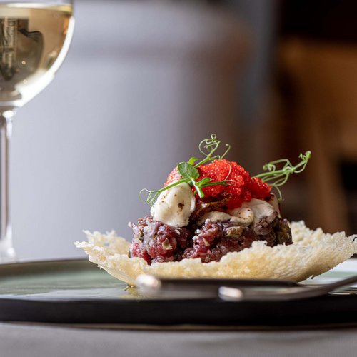 Jesacherhof: Gourmethotel in Österreich Gourmetgericht mit rohem Fleisch und Fischrogen auf knusprigem Teller mit Weinglas