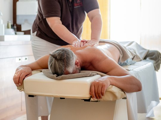 Wellnesshotel im Defereggental: Wohlfühlurlaub vom Feinsten Mann mit Pferdeschwanz bekommt Rückenmassage in hellem Massageraum